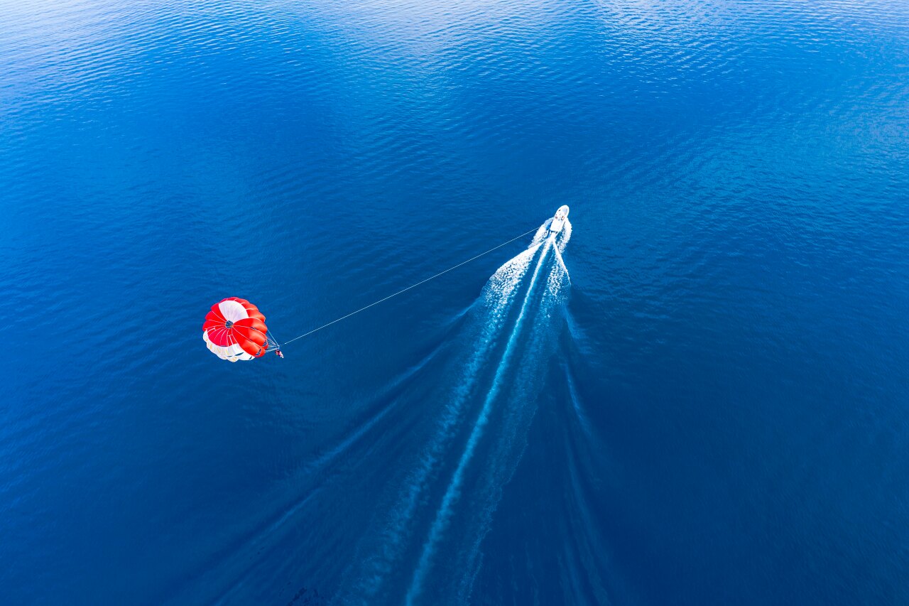 Aerial view of a vibrant red and white parachute being pulled by a speed boat over the deep blue tropical ocean.