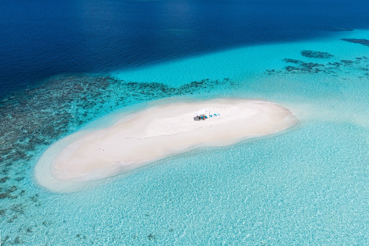 Aerial perspective of a pristine white sandbank surrounded by turquoise lagoon water, perfect for luxury relaxation.