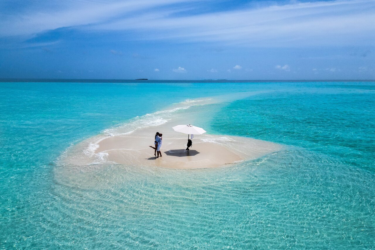 Aerial view of a romantic couple kissing on a pristine white sandbank surrounded by turquoise tropical ocean waters