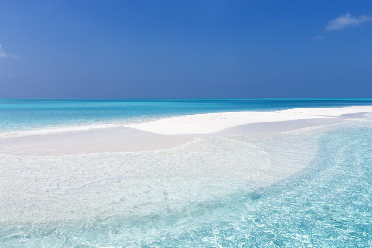 A beautiful white sandbank surrounded by crystal clear turquoise water under a vibrant deep blue tropical sky.