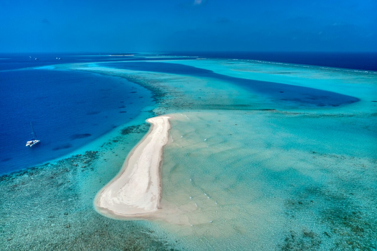 Aerial drone view of a white sandy bank surrounded by turquoise waters with a catamaran anchored nearby for a picnic
