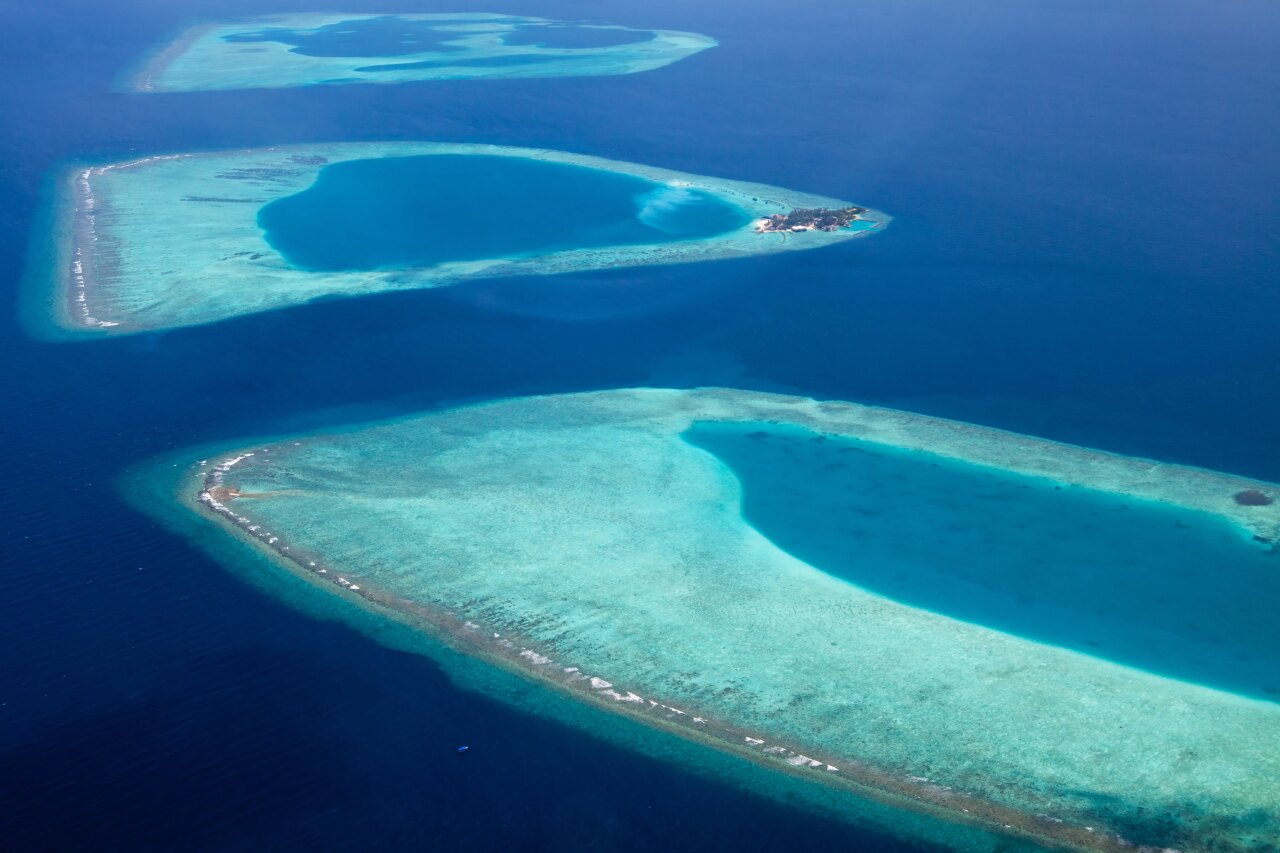Splendida vista aerea dall'alto di vibranti atolli corallini circondati dalle profonde acque blu dell'oceano.