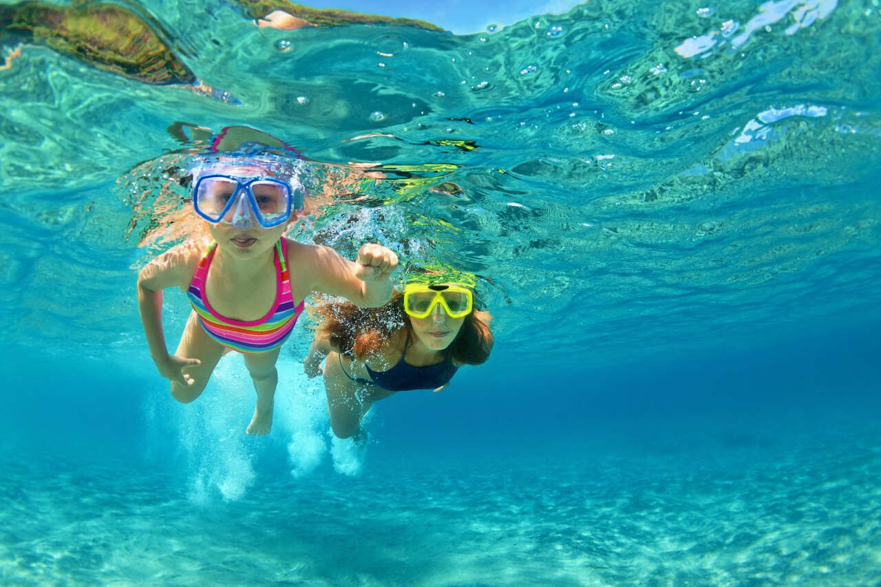 A young girl and her mother snorkeling together in the crystal clear turquoise water of the Indian Ocean.