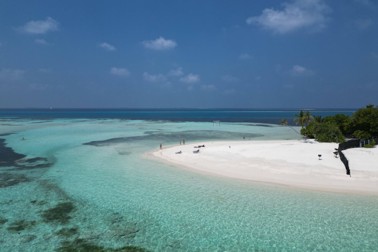 Veduta aerea di una lingua di sabbia bianca sull'isola di Dhangethi con acqua turchese, palme e persone in relax.