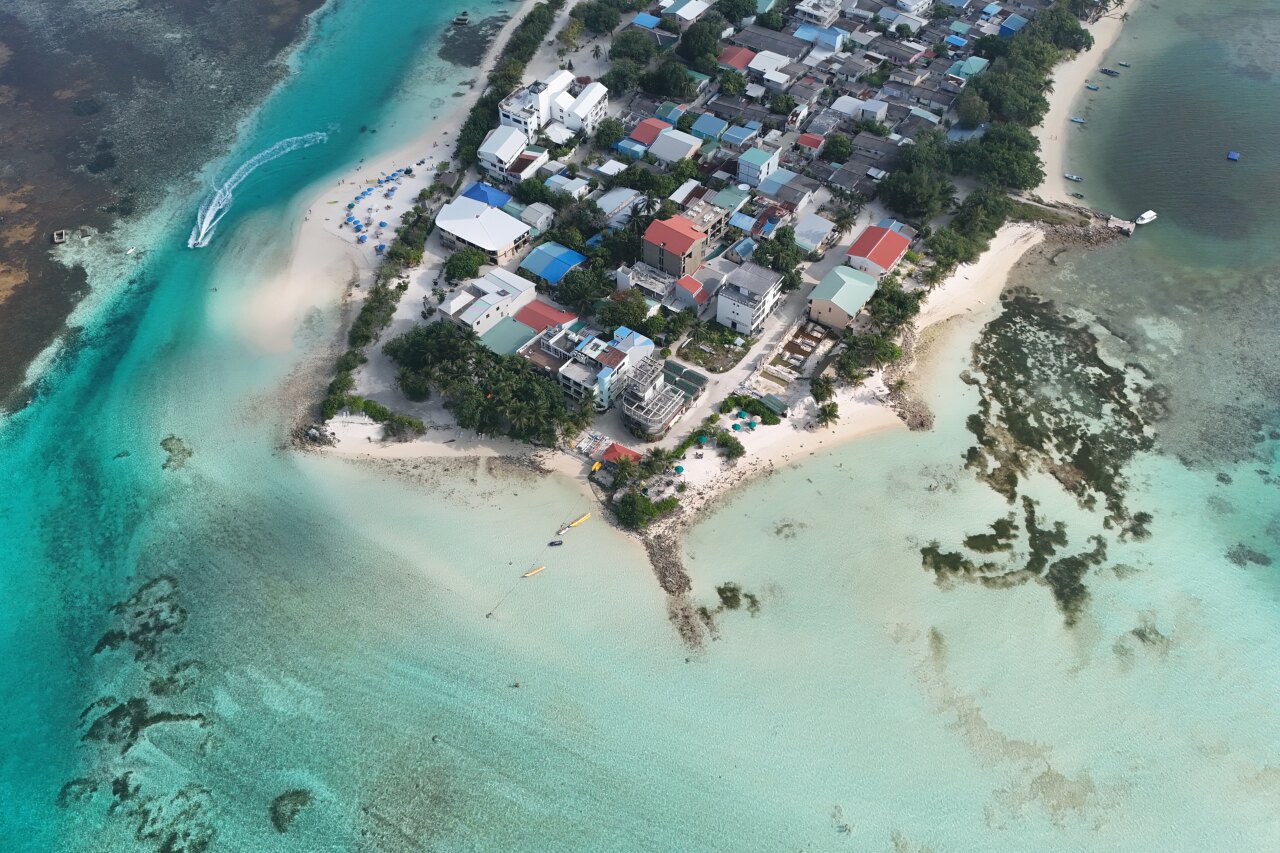 High angle aerial drone perspective of Dhiffushi local island, showcasing the village, sandy beach, and clear lagoon.