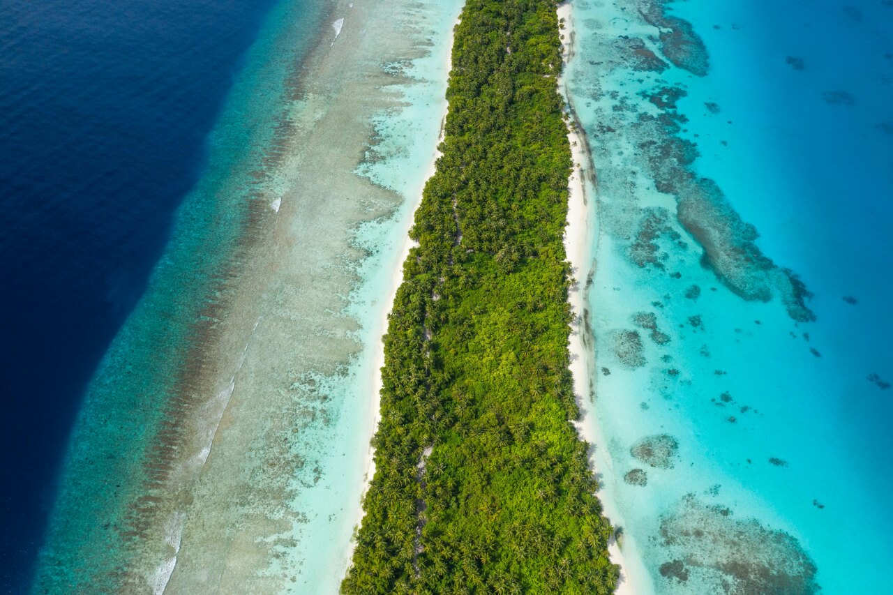 Stunning drone perspective of Dhigurah island, showcasing lush tropical vegetation surrounded by turquoise reefs.