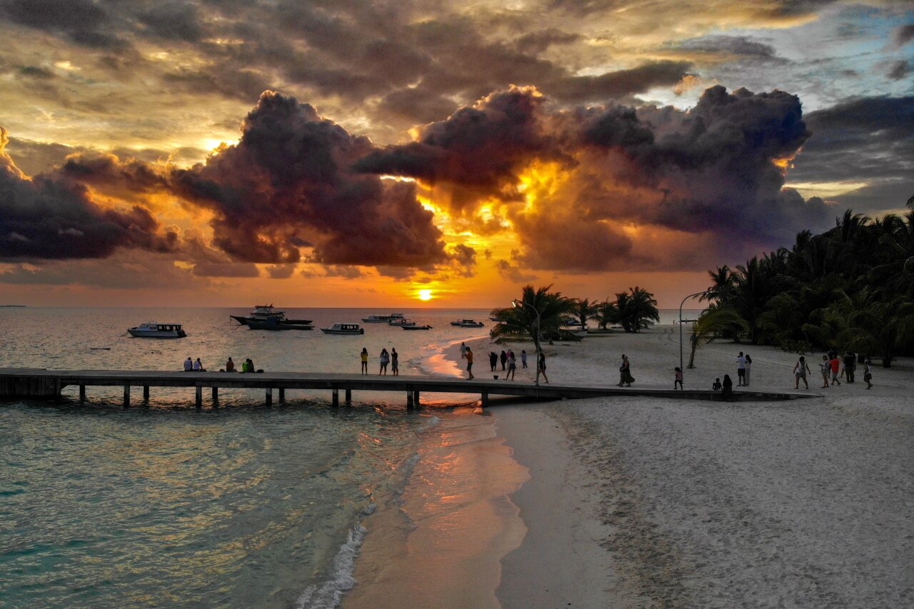 Veduta aerea del molo in legno sull'isola di Fulidhoo, atollo di Vaavu, con persone che ammirano il tramonto dorato