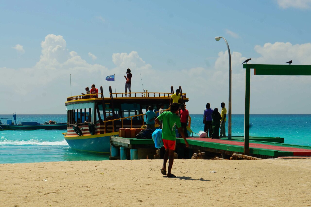 A colorful local wooden ferry docked at a green wooden pier with passengers boarding under a bright sunny sky