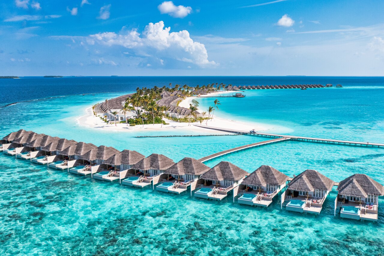Stunning aerial perspective of a tropical overwater resort featuring private villas over turquoise ocean waters.
