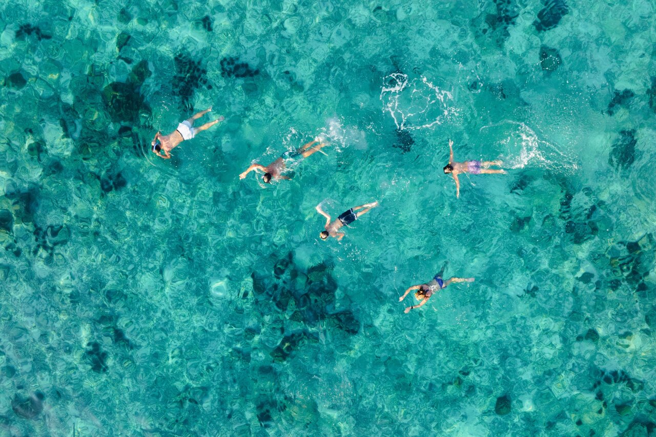 Aerial drone shot of a group of people swimming and snorkeling in the turquoise tropical ocean over a coral reef.