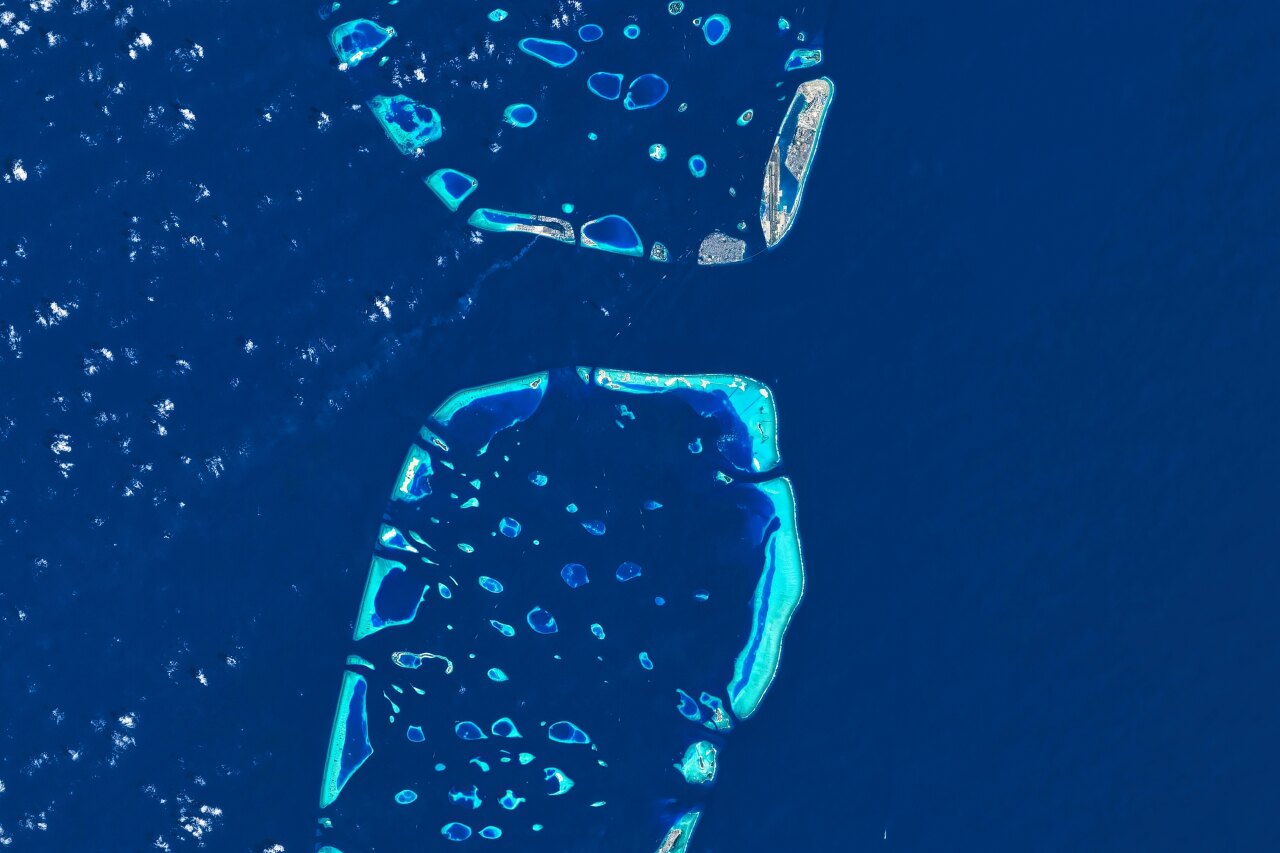 Veduta aerea satellitare ad alta quota che mostra l'acqua blu cristallina dell'oceano che circonda piccoli atolli corallini.