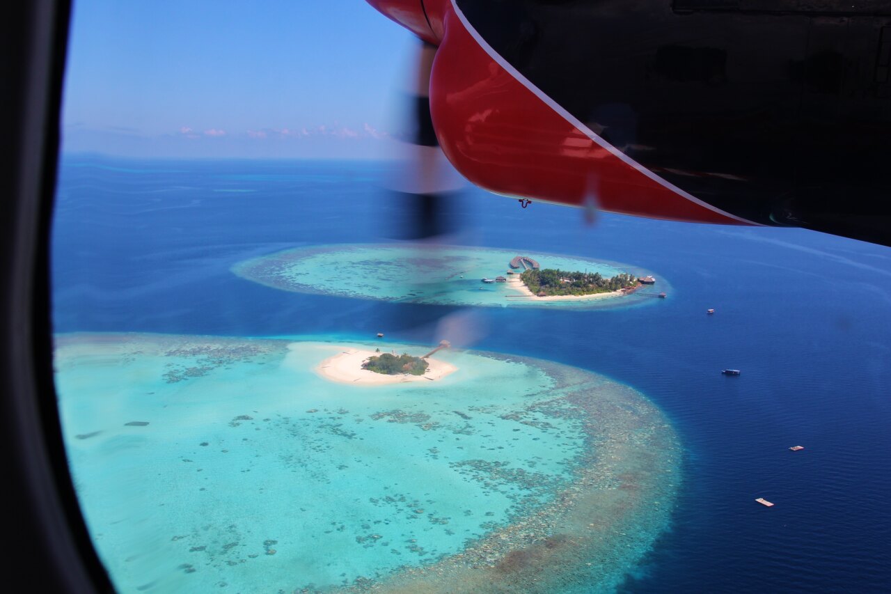 Vista dal finestrino di un idrovolante su piccole isole con lagune turchesi e barriere coralline nel mare profondo.