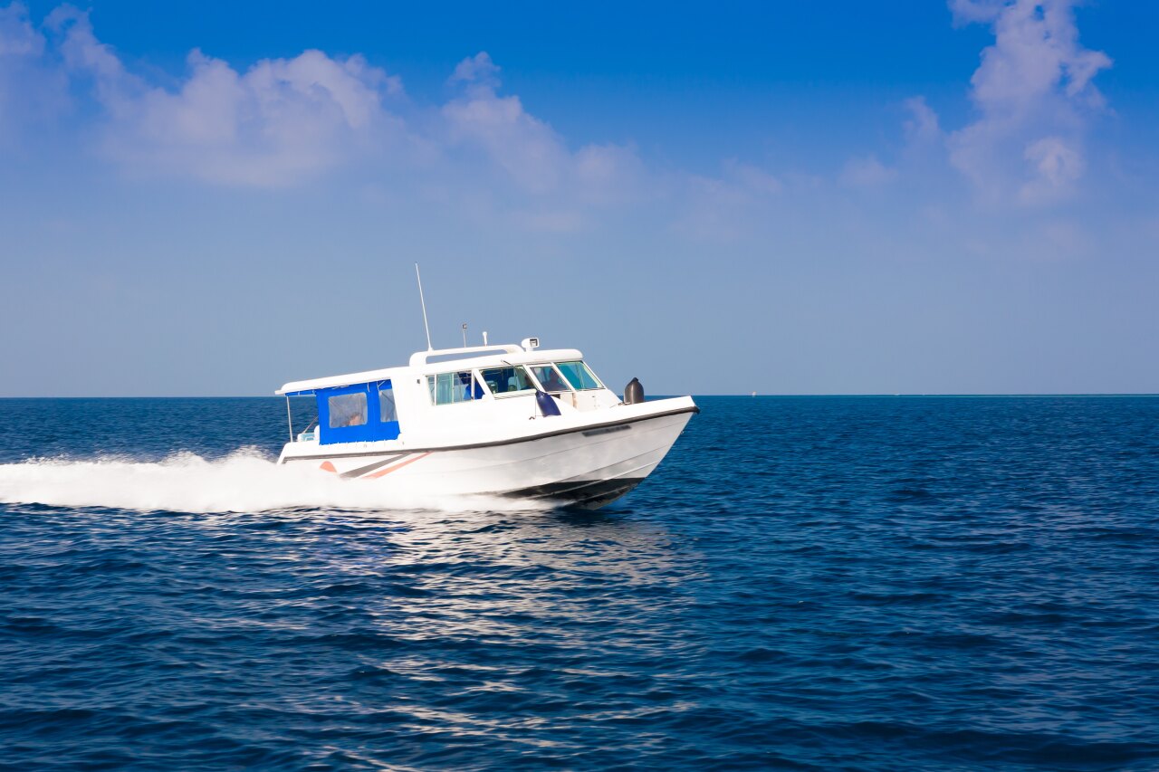 A white speedboat cruising fast across the vibrant blue tropical ocean on a sunny day with clear skies above