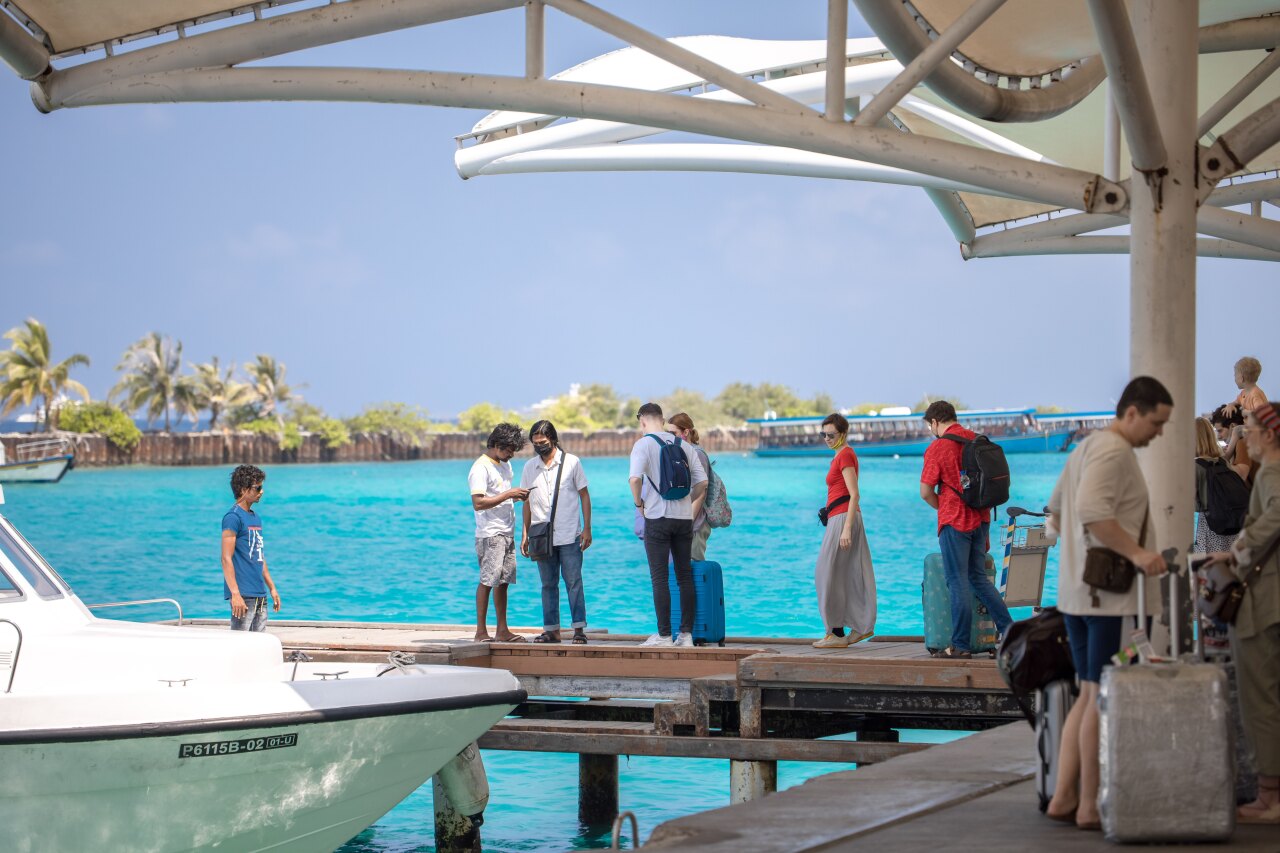 A group of international tourists standing with their luggage on a wooden jetty waiting to board a speedboat