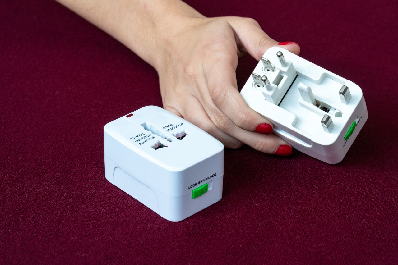 Una persona che tiene in mano un adattatore universale da viaggio bianco con diverse configurazioni di spine.
