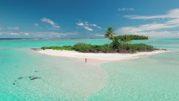 activity, beach, drone-shot, nature, sea - Aerial view of a woman standing on a remote white sandbar surrounded by turquoise ocean during a private picnic.