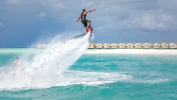 activity, resort - An athlete performs a high jump on a flyboard above the turquoise water with luxury villas in the background
