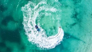activity, drone-shot, sea - Aerial view of a person using a flyboard connected to a jet ski in the turquoise crystal clear waters of the ocean.