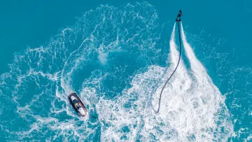 activity, drone-shot - Aerial view of a person using a flyboard connected to a jet ski in the crystal clear turquoise water of the ocean.