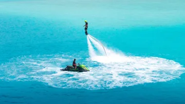 activity, resort, sea - A person performing a flyboard stunt above the turquoise water with an instructor on a jet ski at a luxury resort.