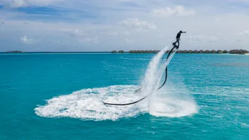 activity, resort - A person soaring high above the turquoise sea on a flyboard, performing exciting water sports near a luxury resort.