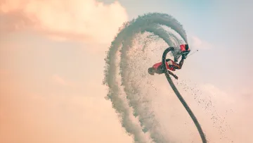 activity, sea - A professional athlete performs an acrobatic stunt on a flyboard, suspended above the ocean with water spray jets.