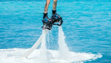 activity - A person wearing a life jacket and boots flying above the turquoise sea using a powerful flyboard water jet equipment.