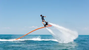 activity - A man in a helmet and wetsuit performing a flyboard stunt above the blue tropical ocean on a sunny day in the Maldives.