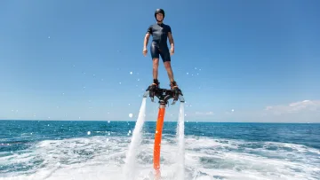 activity - A man in a wetsuit performing an exciting flyboard stunt above the crystal clear blue ocean waters on a sunny day.