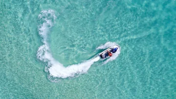 activity, drone-shot, sea - Aerial view of a tourist enjoying a high-speed jet ski ride creating a wake in clear turquoise tropical ocean waters.