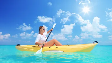 activity, sea - Una donna con occhiali da sole rema su un kayak giallo nelle acque turchesi e cristalline sotto un cielo soleggiato