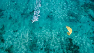 activity, drone-shot, sea - Aerial drone shot of a kitesurfer gliding over the turquoise waters of the lagoon with a vibrant yellow kite.