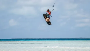 activity, sea - A professional kitesurfer performing a high jump over the turquoise shallow waters of a tropical island beach.