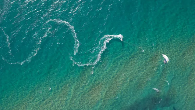 activity, drone-shot, sea - Aerial drone shot of a kitesurfer gliding over turquoise tropical waters leaving a long curved white wake behind.
