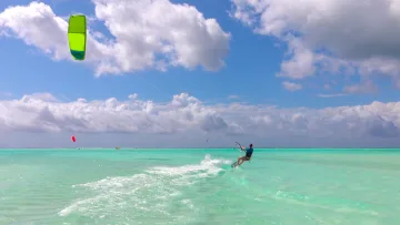 activity, sea - A man enjoying kitesurfing on the crystal clear turquoise water of the ocean under a bright cloudy blue sky.