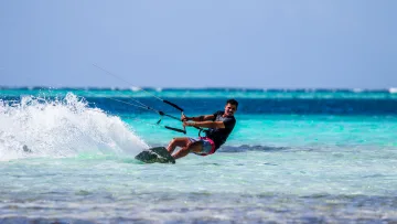 activity, people, sea - A smiling man kitesurfing across the turquoise tropical waters, showing an exciting and dynamic water sports action.