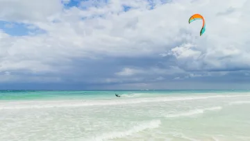 activity, sea, sky - A kitesurfer gliding across the vibrant turquoise ocean under a dramatic cloudy sky in the tropical islands.