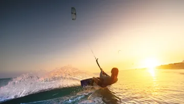 activity, sunset - A woman enjoying a kitesurfing session on tropical waters, carving through the waves during a golden sunset.