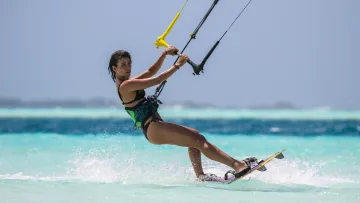 activity, sea - An athletic woman kitesurfing across the turquoise lagoon, holding the control bar with focus and energy.