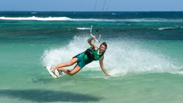 activity, sea - A smiling woman gliding on the surface of turquoise ocean water while practicing kitesurfing on a sunny day