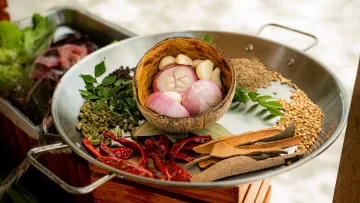 activity, food - A close up view of fresh local spices, onions and garlic arranged in a coconut shell inside a steel pan for cooking.
