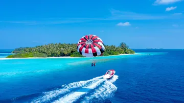 activity, sea - A couple enjoying a parasailing experience towed by a motorboat above the turquoise tropical ocean waters.