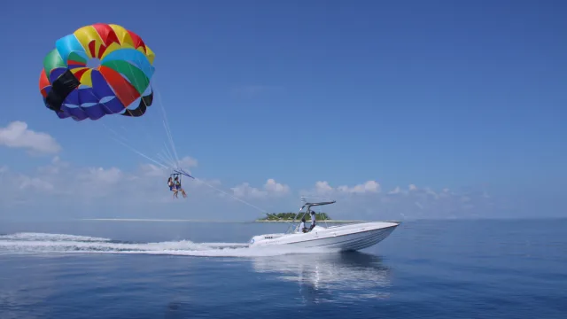 activity - A couple enjoying a tandem parasailing flight pulled by a speedboat over the deep blue tropical ocean waters.