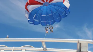 activity, sky - A couple enjoying a tandem parasailing flight high in the blue sky above the clear tropical sea of the Maldives.