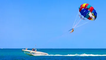 activity, sea - A person enjoys parasailing in the sky above the deep blue ocean, pulled by a speedboat on a clear sunny day.