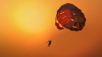 activity, sky, sunset - A silhouette of a person parasailing high above the ocean against a vibrant golden sunset in the Maldives sky.
