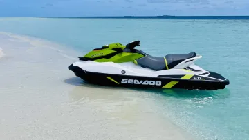 activity, beach, sea - A green and white Sea-Doo jet ski parked on the white sandy shore against the turquoise waters and blue sky.