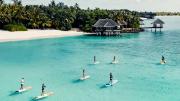 activity, people, sea - Gruppo di persone in Stand Up Paddle su acque turchesi cristalline con ville su un'isola tropicale sullo sfondo.