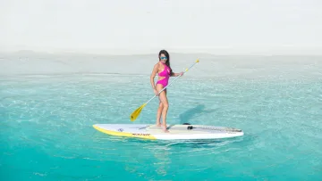 activity, beach, people, sea - Una donna in costume rosa pratica stand up paddle su una tavola Naish nelle limpide acque turchesi dell'oceano.