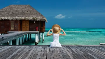 activity, accommodation, luxury, resort, sea - Una donna con abito bianco e cappello di paglia seduta su un pontile di legno ammira il mare turchese vicino alla villa.